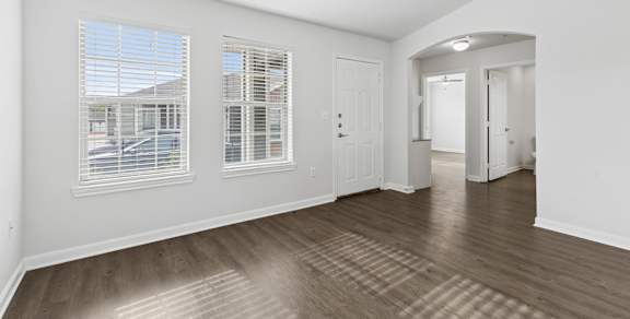 an empty living room with a ceiling fan and three windows
