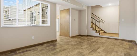 A room with wooden flooring and a staircase leading to another room.