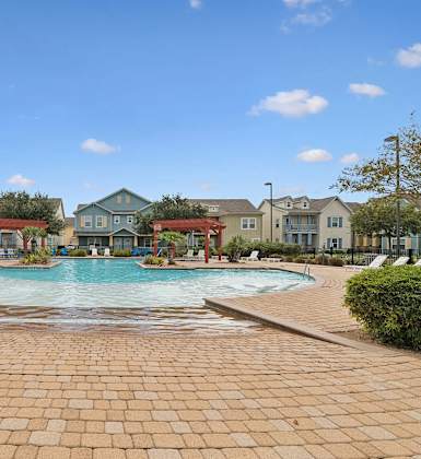 A swimming pool surrounded by a brick walkway in front of a row of houses.