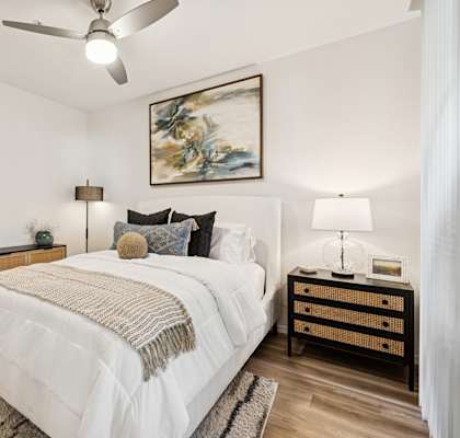 A bedroom with a large bed, a ceiling fan, and a painting on the wall.