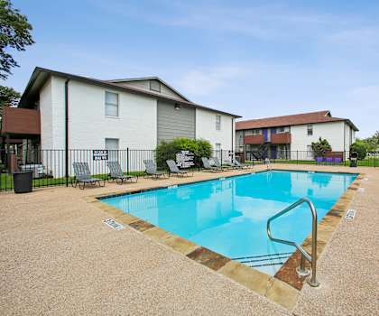 A swimming pool surrounded by lounge chairs and apartment buildings.