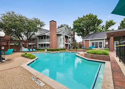 A pool surrounded by a brick patio and a black fence.