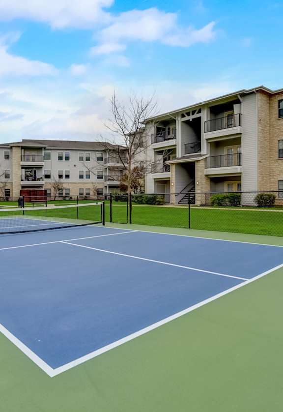 A tennis court is surrounded by apartment buildings.