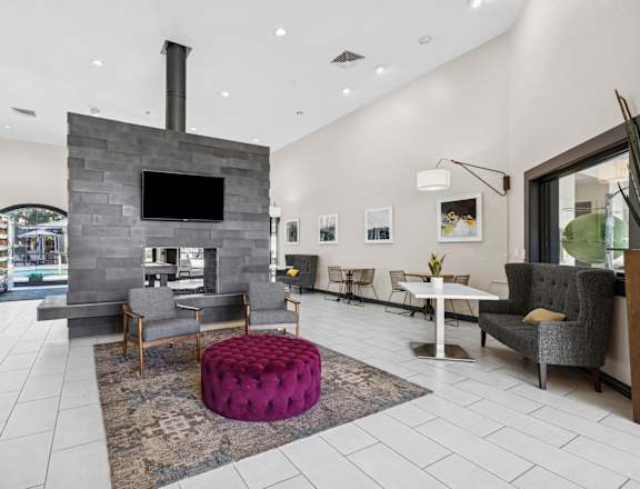 A modern living room with a stone fireplace and a purple ottoman.