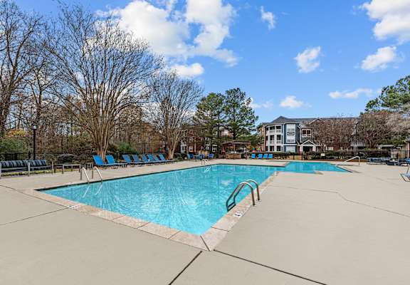 A large swimming pool surrounded by trees and chairs.