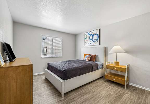 A bedroom with a bed, nightstand, and a painting on the wall.