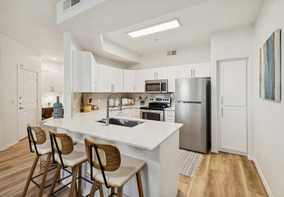 A modern kitchen with a white countertop and wooden chairs.
