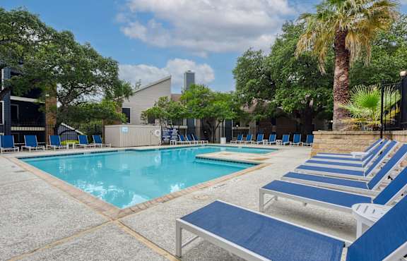 A pool surrounded by blue lounge chairs and palm trees.
