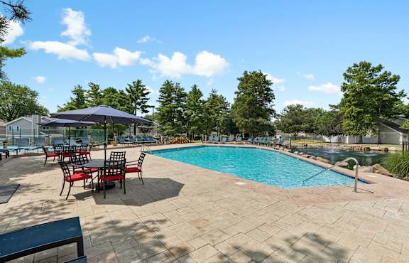 A pool surrounded by trees and chairs.