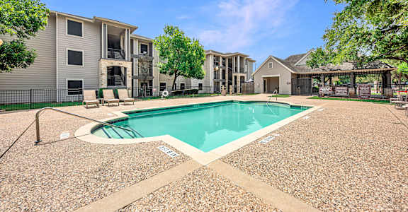 A swimming pool surrounded by a gravel area and apartment buildings.