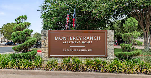 A sign for Monterey Ranch Apartment Homes is displayed in front of some trees.