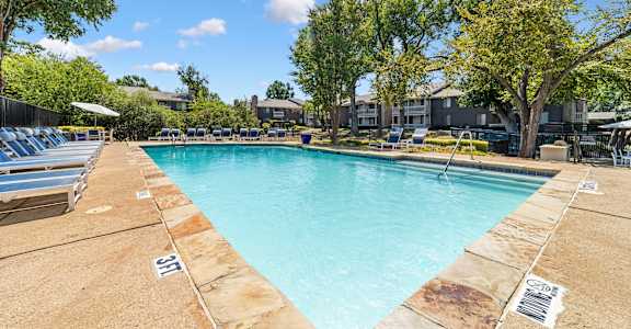 A large swimming pool surrounded by trees and lounge chairs.