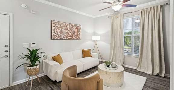 A living room with a white couch, a brown chair, and a ceiling fan.