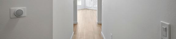 a long hallway with white walls and wood flooring and a door in the background