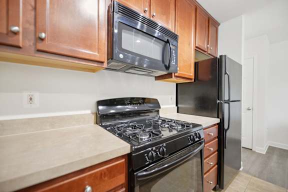A kitchen with a black refrigerator, black stove, and black microwave above a counter with a beige countertop.