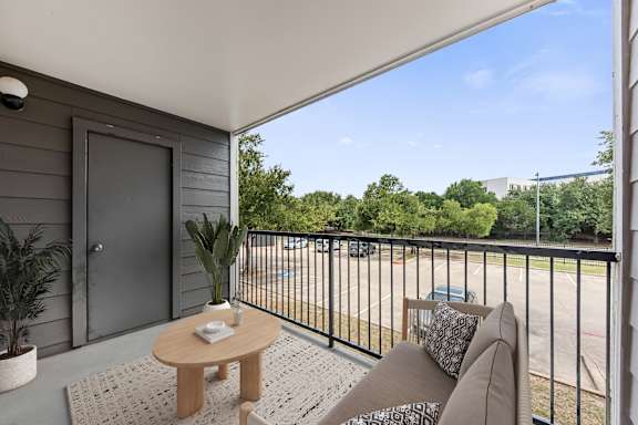 A balcony with a table and chairs overlooking a parking lot.