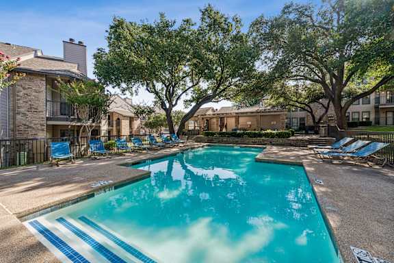 A swimming pool surrounded by trees and chairs.