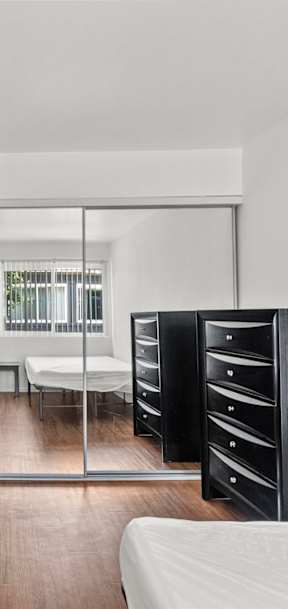 A bedroom with mirrored closet doors, dressers, and beds