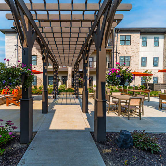 A patio with a pergola and chairs is surrounded by a building.