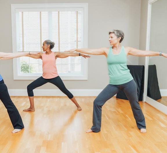 Three women are practicing yoga in a room with wooden floors.
