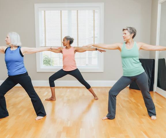 Three women are practicing yoga in a room with wooden floors.