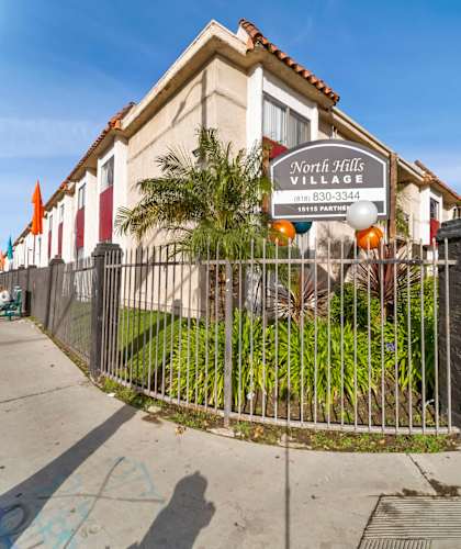 A sign for North Hills Village with a phone number is displayed on a fence.