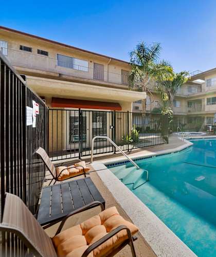 A sunny day at a poolside with chairs and apartment buildings in the background.