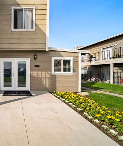 A building with a white door and windows with flower beds in front.