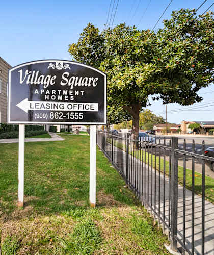 A sign for Village Square Apartments is in front of a building.