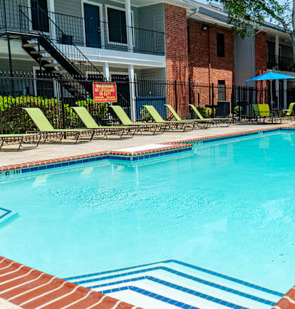 A swimming pool surrounded by a brick border and lounge chairs.