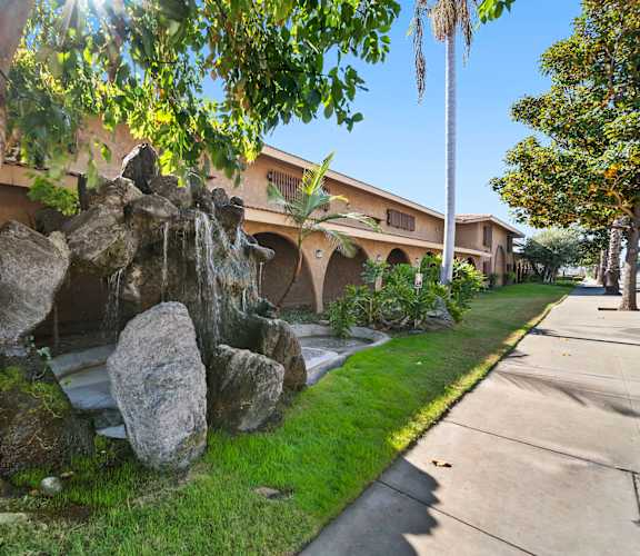 A large rock formation is in the foreground of a building with a waterfall feature.