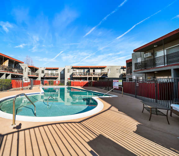 A swimming pool surrounded by a wooden deck and buildings.