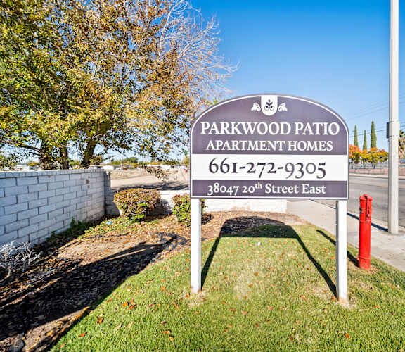 A sign for Parkwood Patio Apartment Homes stands in front of a tree.