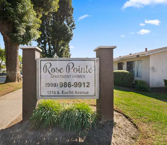 A sign for Rose Pointe Apartment Homes stands in front of a tree.