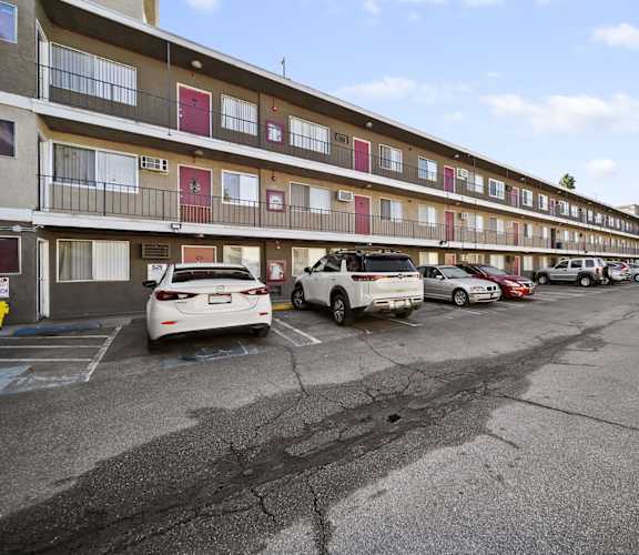 A parking lot in front of a multi-story apartment building with cars parked.