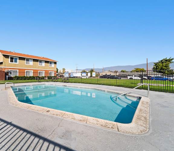 A small pool in a concrete area with a building in the background.