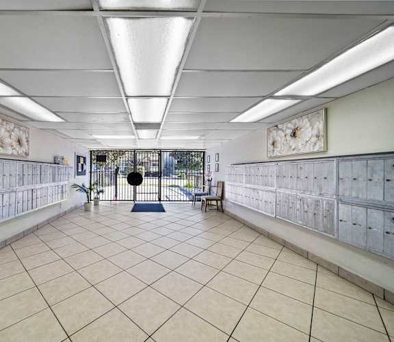 A room with a white tile floor and walls, with a row of mailboxes on the walls and a bench in the middle.