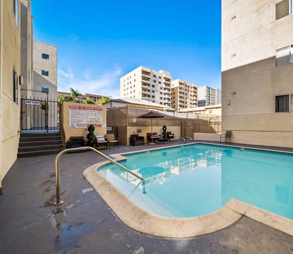 A small pool with a diving board is surrounded by buildings.