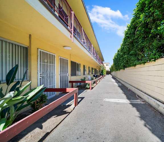 A yellow building with a red railing and a green plant on the side.