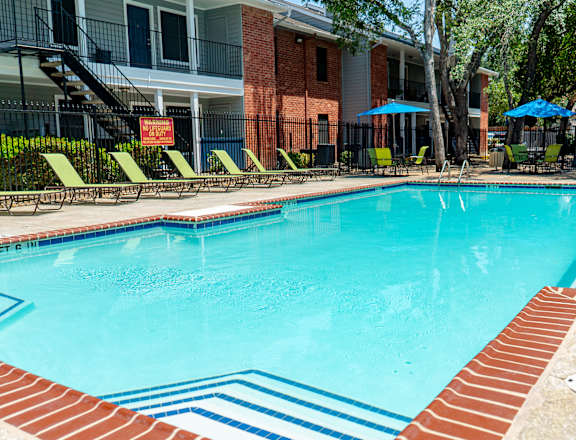 A swimming pool surrounded by a brick border and lounge chairs.