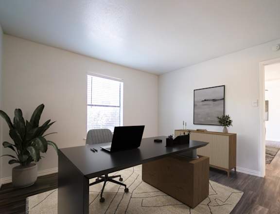 A room with a desk, laptop, and potted plant.