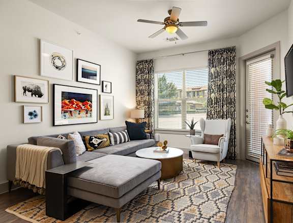 A living room with a grey couch, a coffee table, a television, and a ceiling fan.