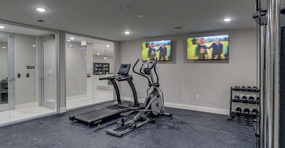 a home gym with exercise equipment and two televisions on the wall