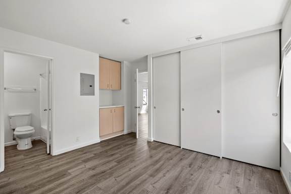 a living room with white walls and wooden floors and a toilet