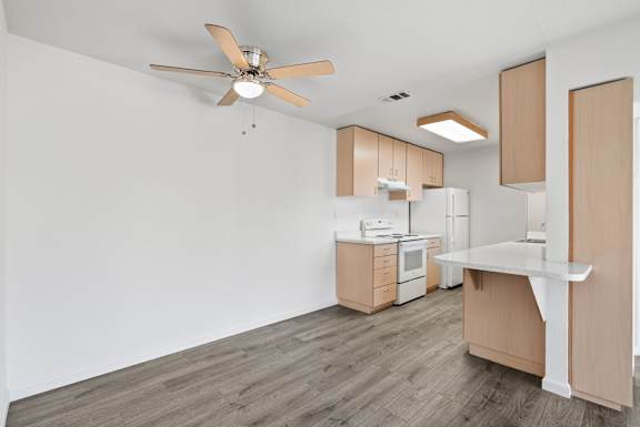 a kitchen with white walls and wood flooring and a ceiling fan