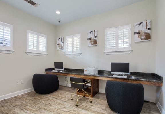 a desk with two computers and two chairs in a room with white walls and white shutters