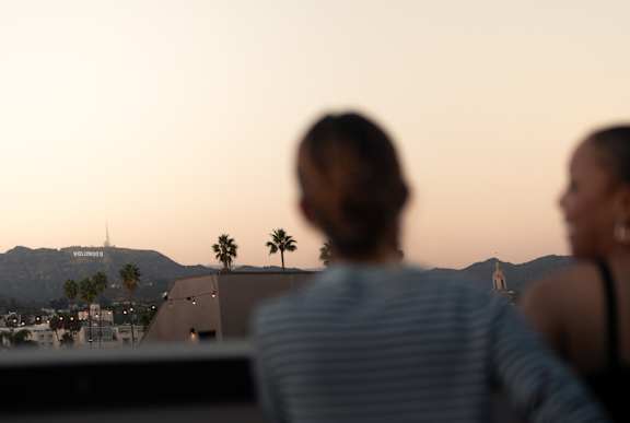 Two people are sitting in front of a sunset with the Hollywood sign in the distance. at SMB Hollywood Apartments, California, 90038