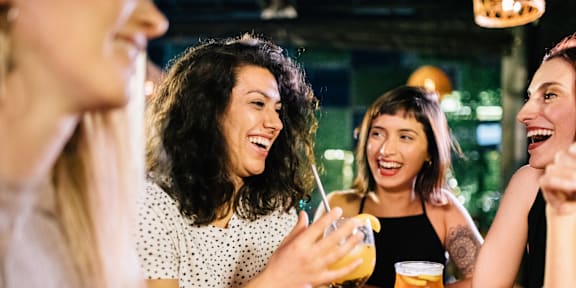 A group of people are sitting around a table, laughing and enjoying drinks.