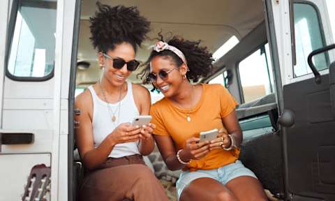 Two women sitting in a van looking at their phones.