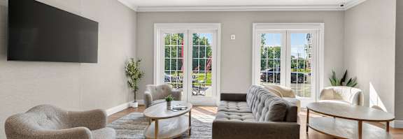 A living room with a grey couch, a grey armchair, a grey rug, a wooden coffee table, a wooden side table, a wooden floor, a wooden TV stand, a wooden floor lamp, a wooden floor, a wooden wall